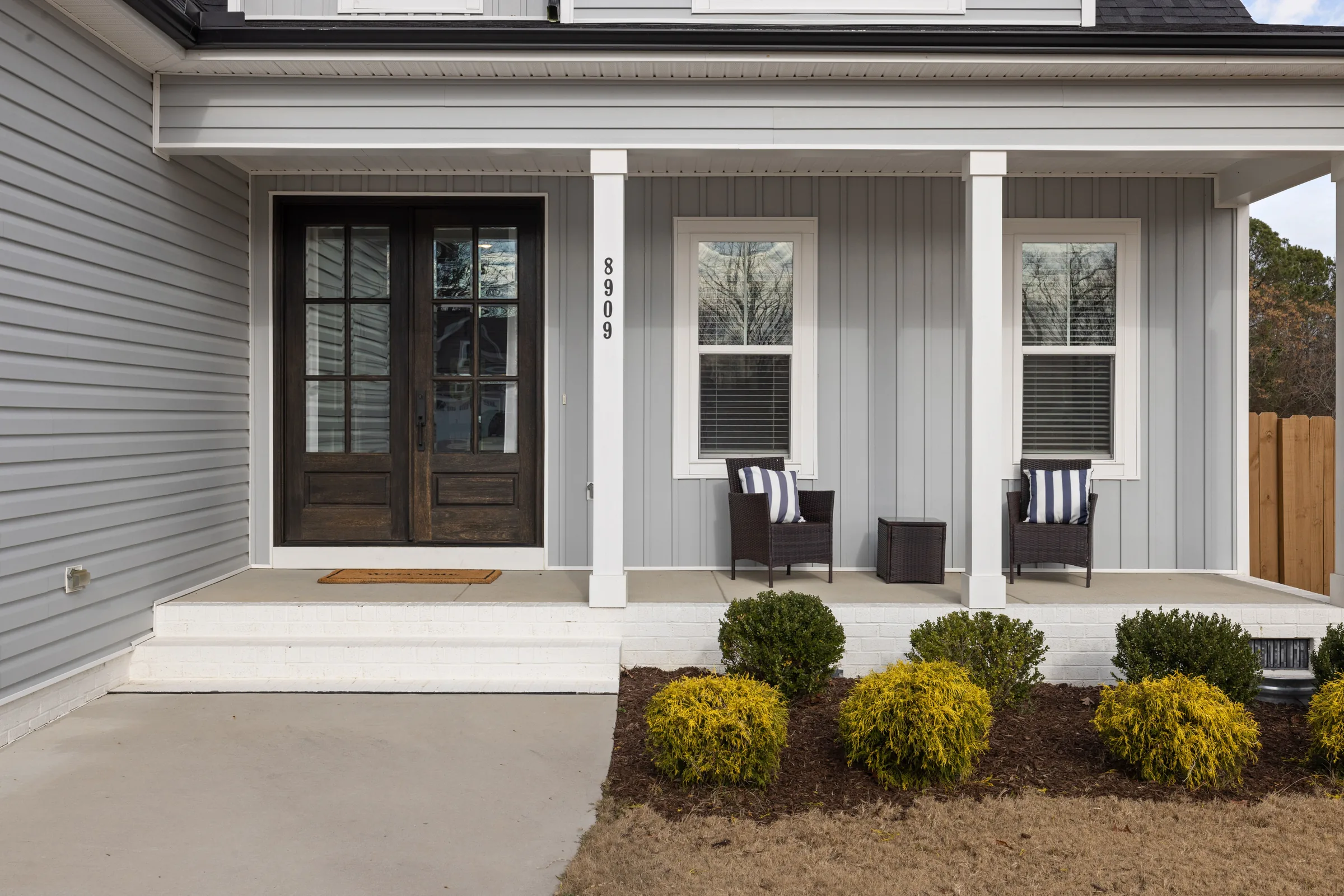 Gray bungalow porch with dark wooden double doors and garden shrubs