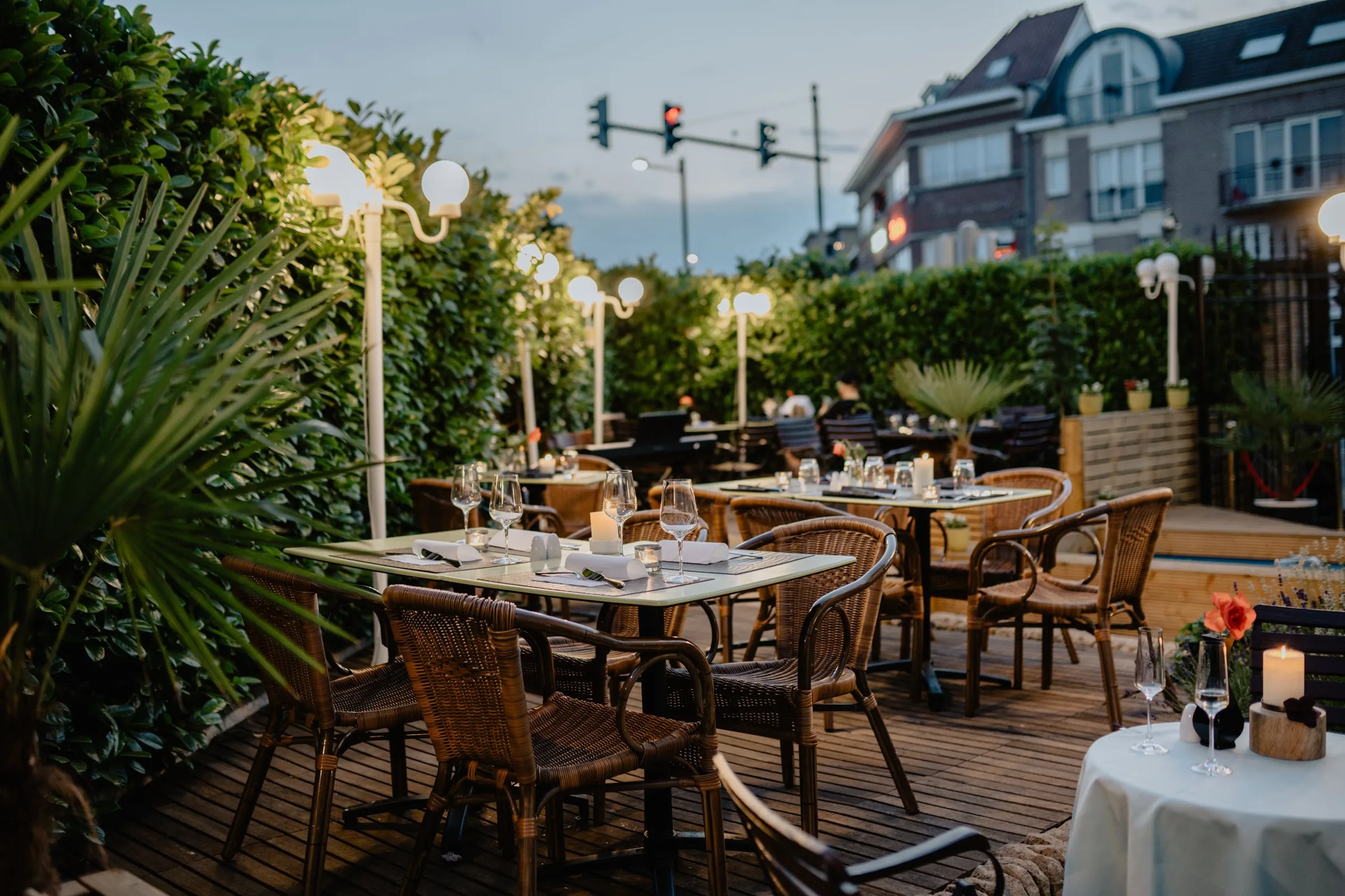 Garden restaurant terrace with candlelit tables surrounded by dense greenery at dusk