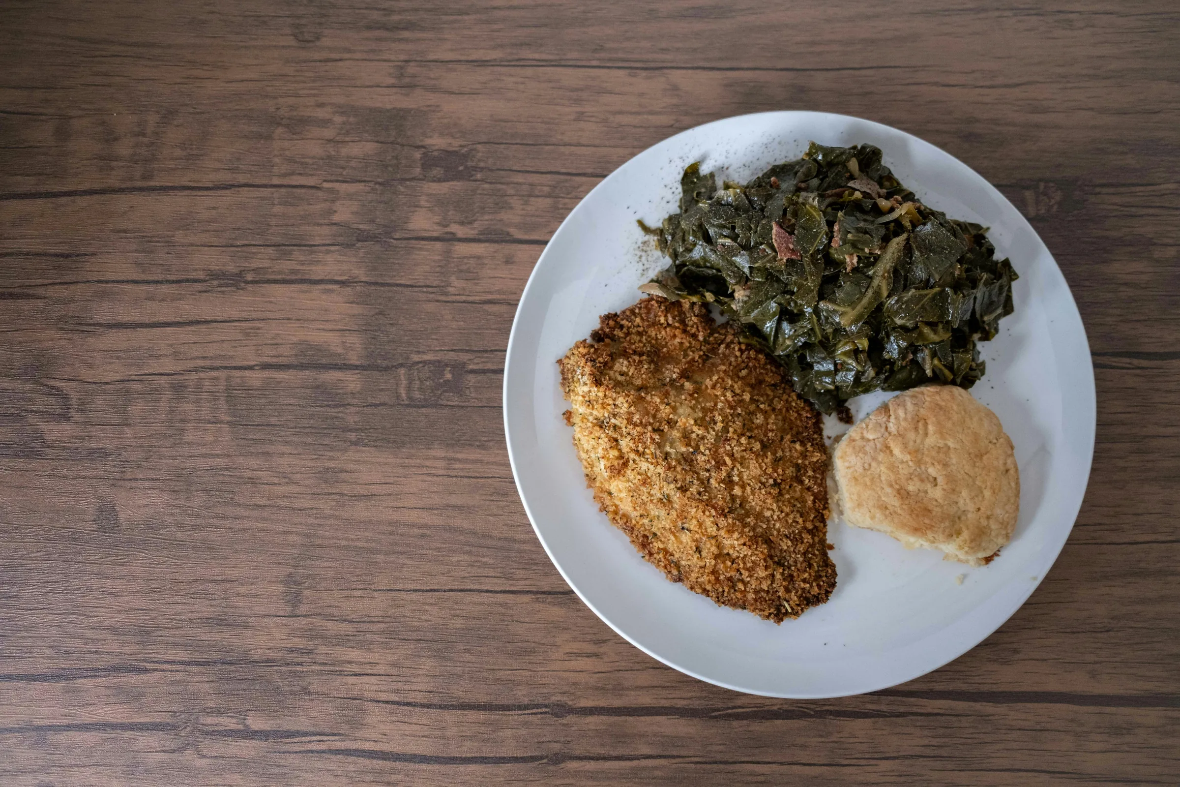 Southern comfort plate with breaded fish, collard greens, and a biscuit on a wooden table